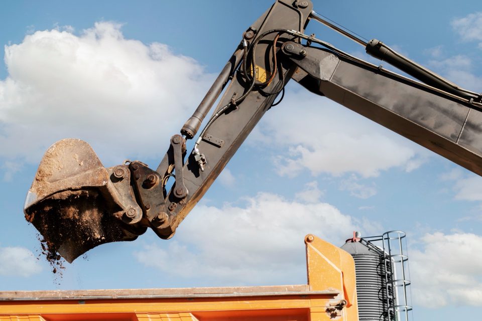 Grävmaskinsarm med hydraulcylindrar och skopa mot en blå himmel