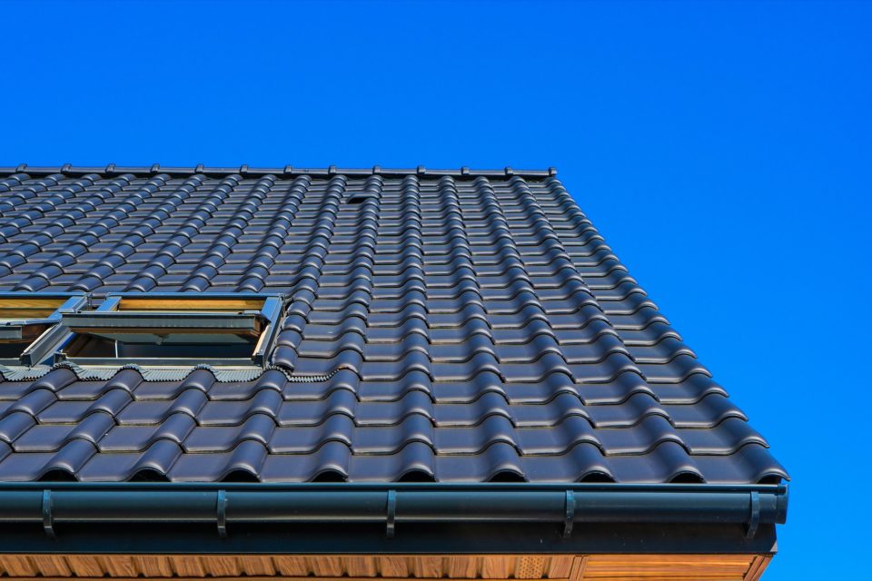 Takränna längs takfoten på ett mörkt pannetak mot blå himmel